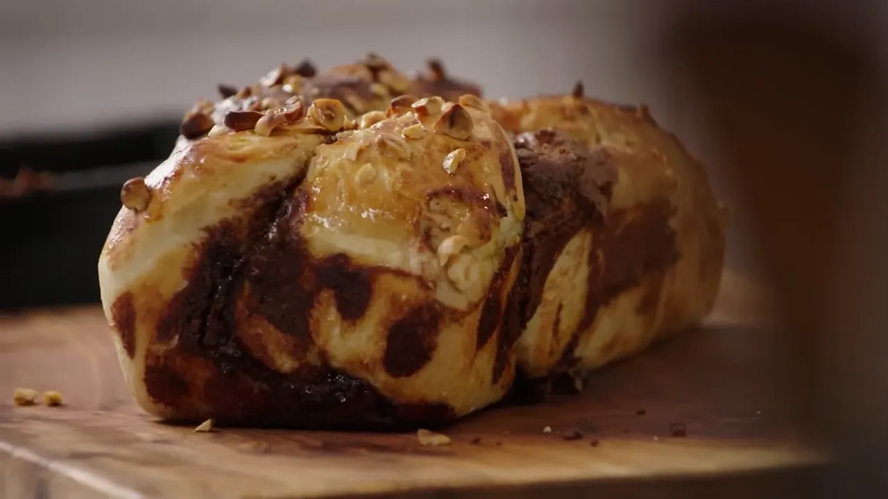 Chocolate twister loaf with a glossy egg-wash crust and chopped hazelnuts on a wooden board