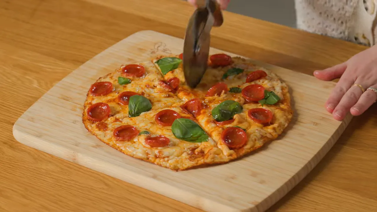 One‑pan pepperoni pizza on a wooden cutting board being sliced with a pizza cutter.