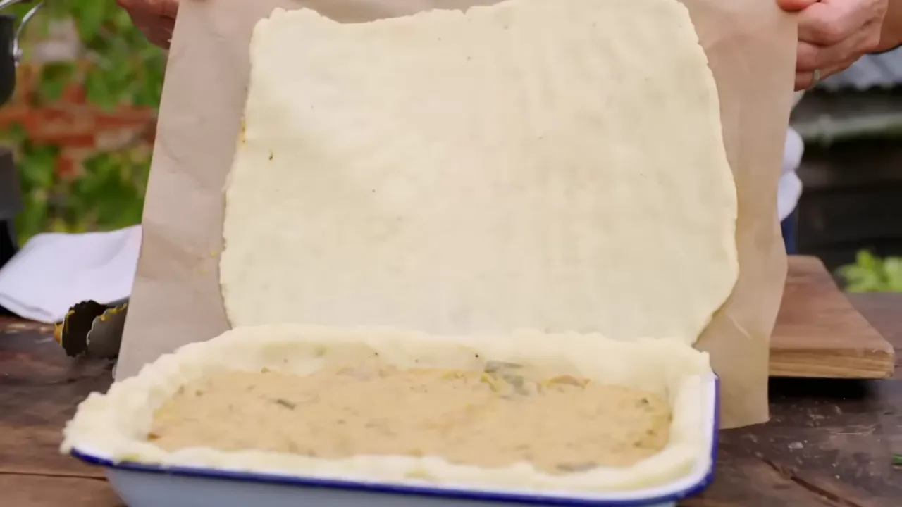 placing mashed potato lid over sausage and leek filling in an enamel pie dish
