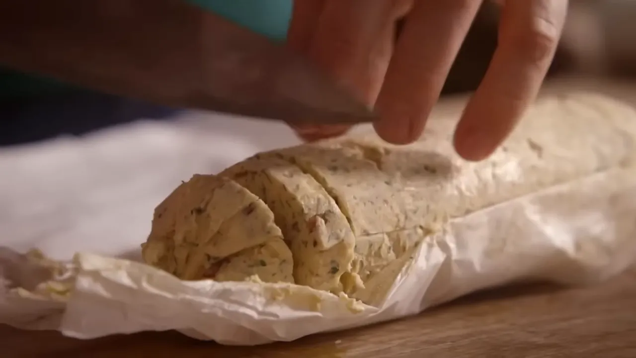 hands slicing a chilled herb and smoked-bacon garlic butter log on parchment