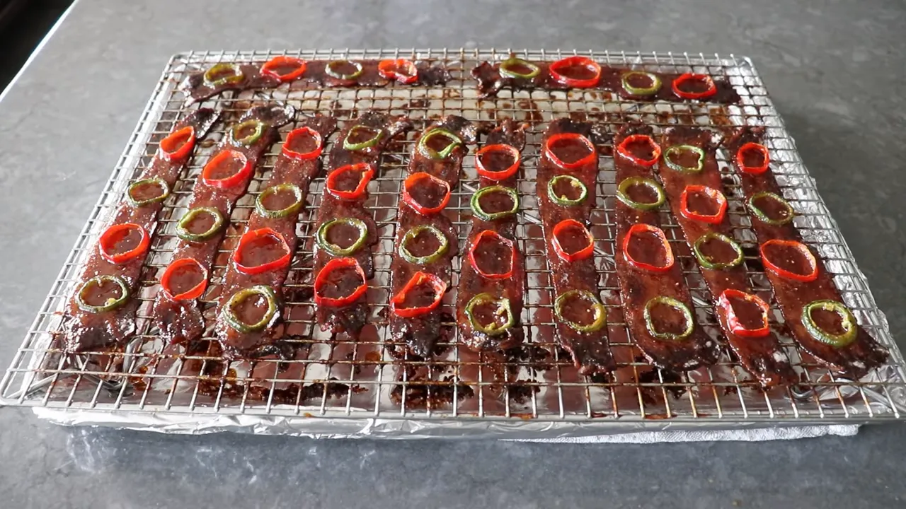Caramelized thick-cut bacon strips topped with red and green pepper rings on a wire rack