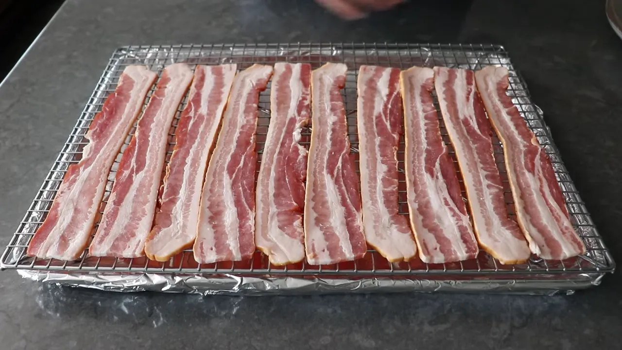 Neatly arranged thick-cut bacon strips on a wire rack above a foil-lined baking sheet