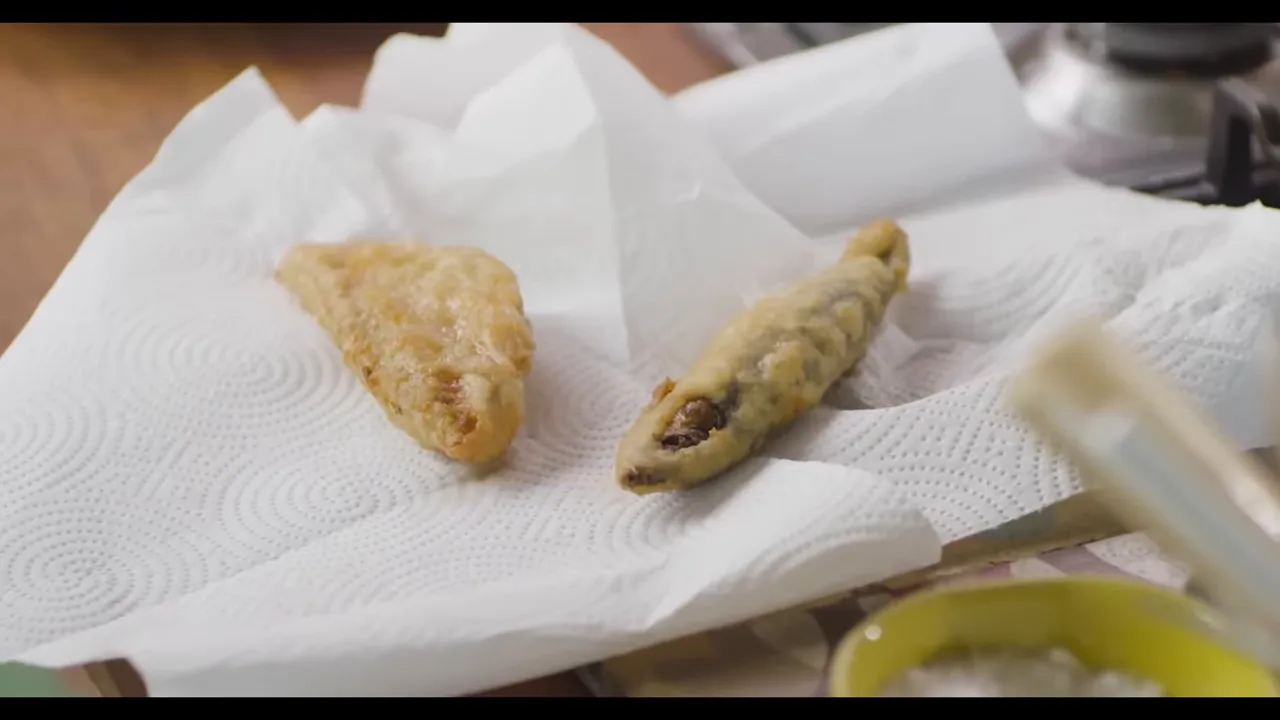 Freshly fried fritto misto pieces on paper towels draining oil, close-up.