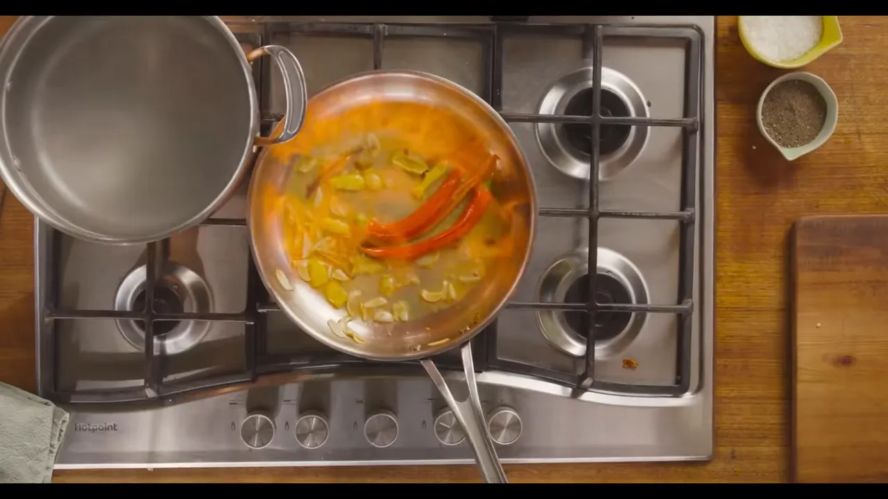 Top-down pan with red chilies and aromatics sizzling on a stove