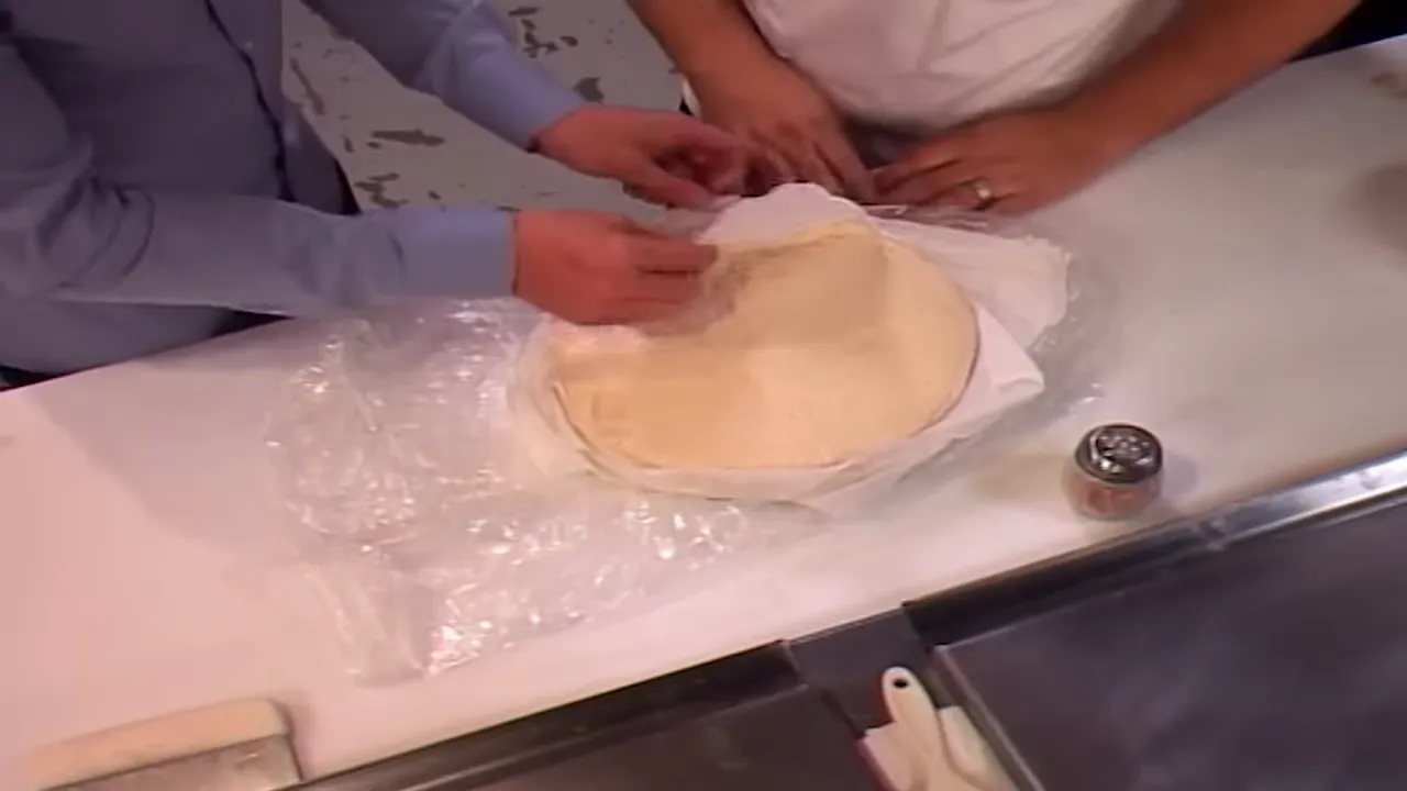 Hands unwrapping and inspecting stacked pizza dough discs on a counter