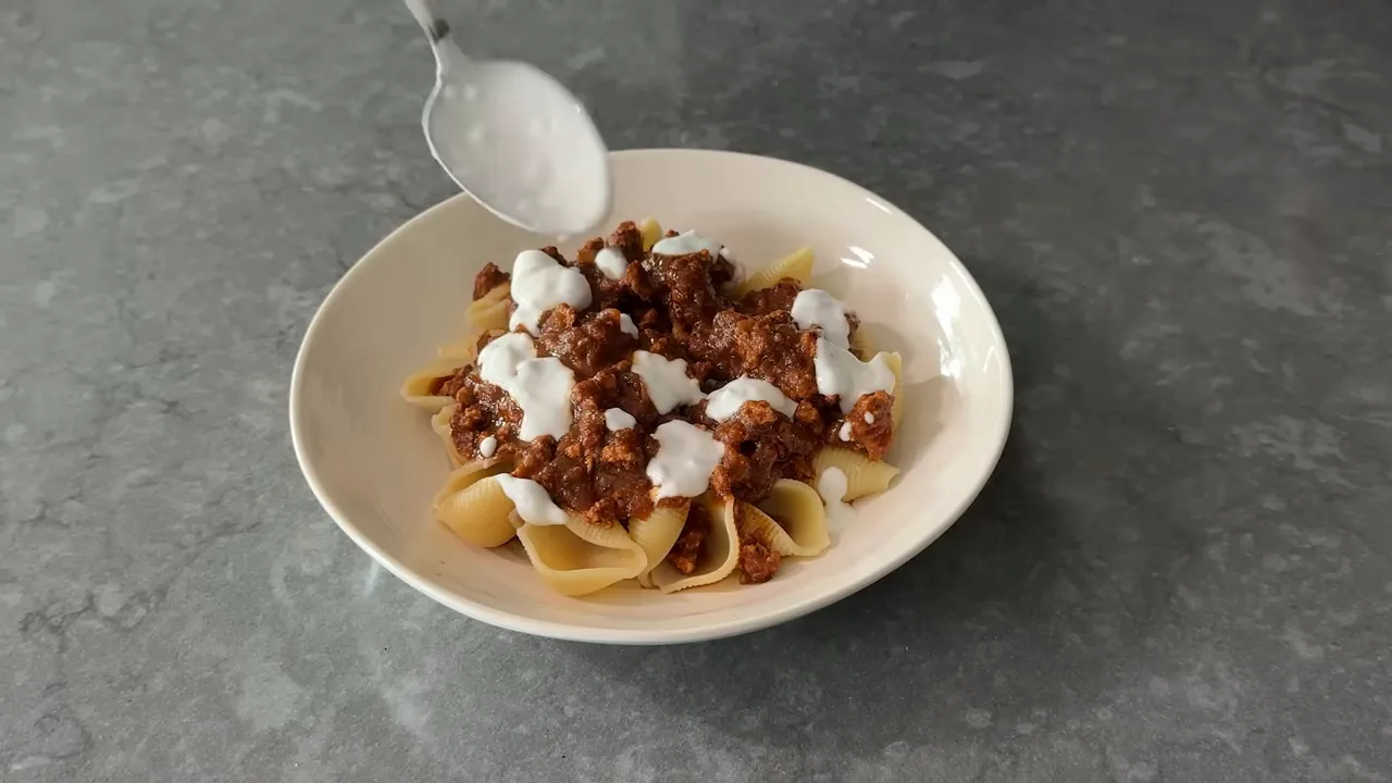 Bowl of shells topped with turkey chili and garlicky yogurt sauce, finished with herbs