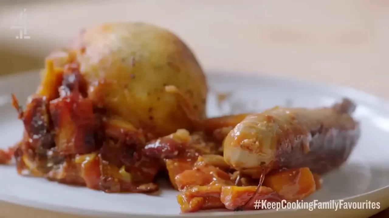 plate showing a browned sausage beside a golden potato dumpling and chunky tomato casserole