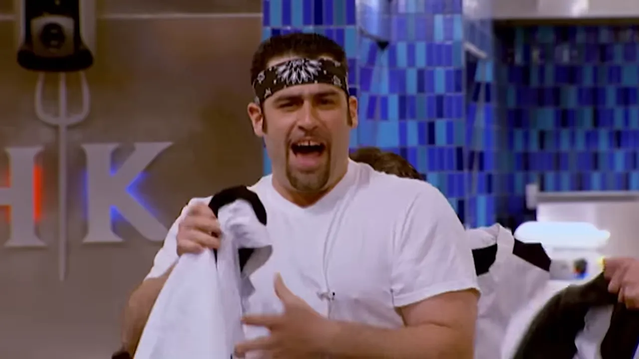 Chef reacting energetically in a Hell's Kitchen cooking station with HK logo in background