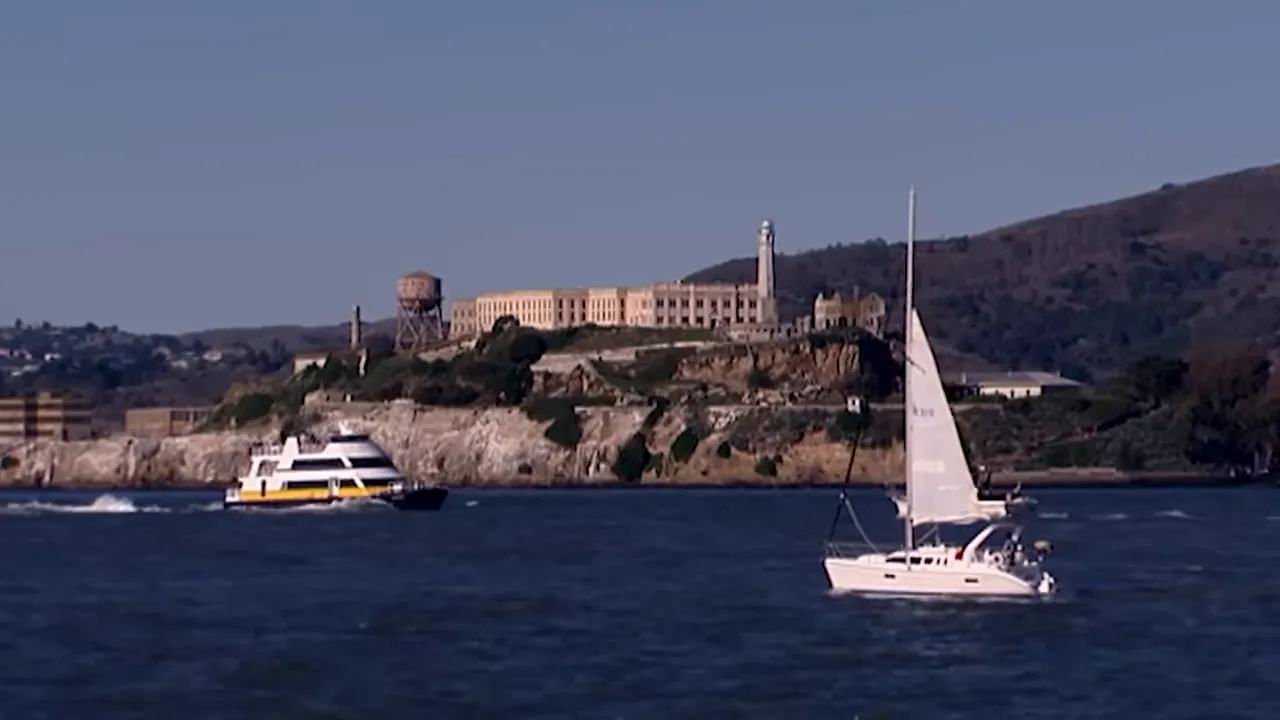 San Francisco Bay with Alcatraz island, a ferry and a sailboat under a clear sky