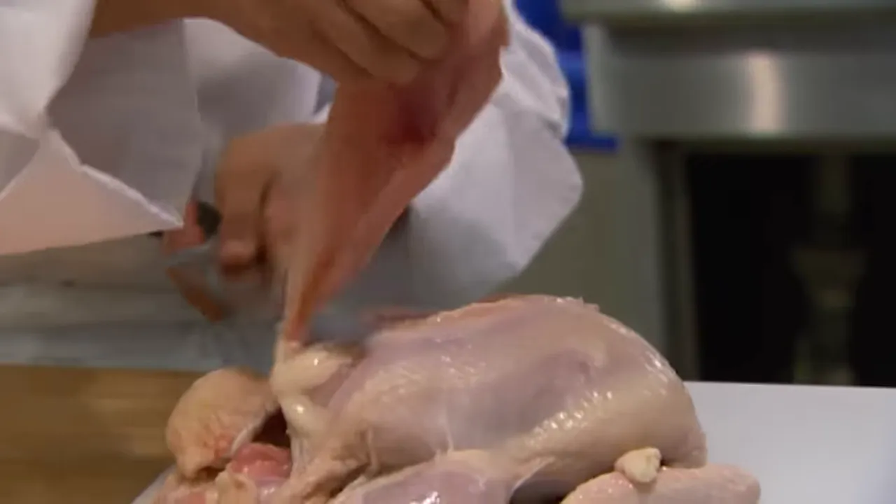 Chef preparing a whole raw chicken on a cutting board, demonstrating butchery technique