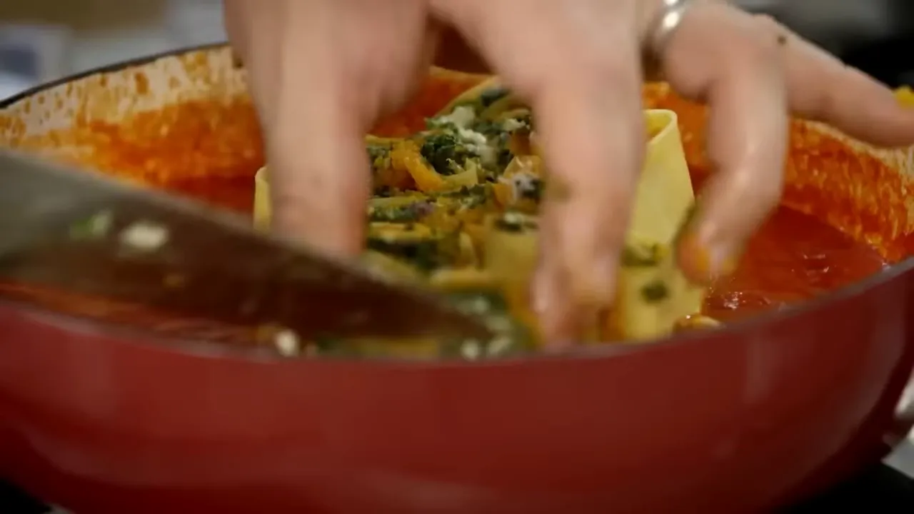 Hands arranging squash and spinach filled rotolo pieces upright in a pan of tomato sauce, ready for baking