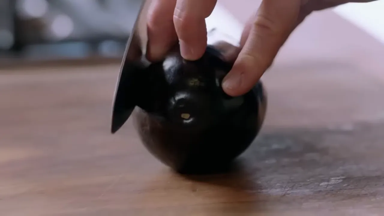 Close-up of a hand using a knife to score an aubergine on a wooden board