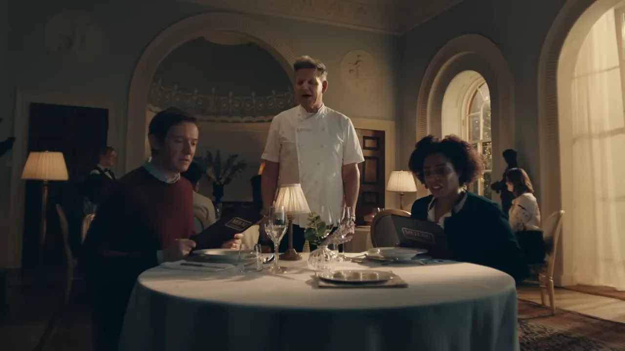 Chef standing at a dining table with guests in a warmly lit restaurant