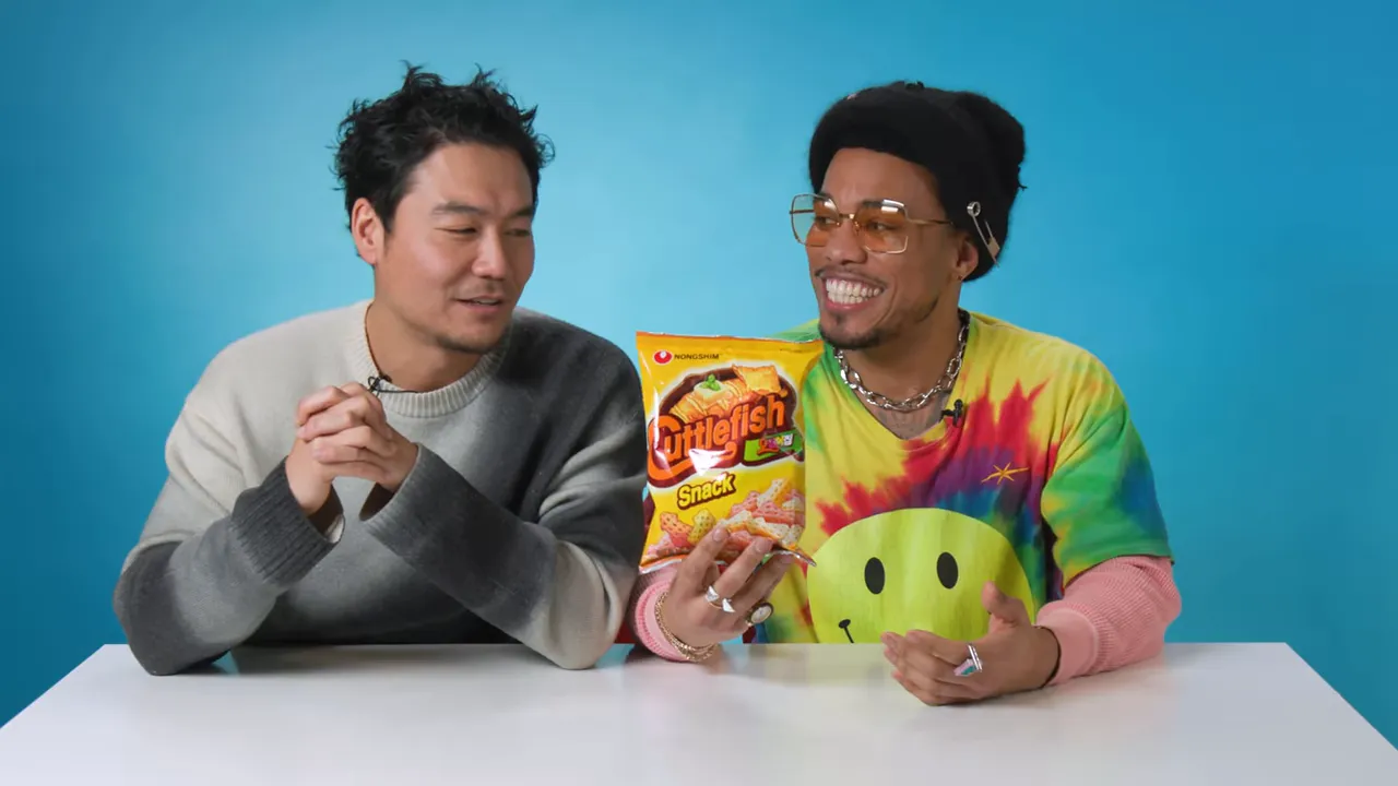 Two hosts at a table presenting a front-facing bag of Cuttlefish chips against a blue background.