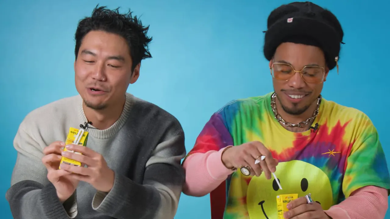 Two hosts smiling as they open and sip banana milk with straws from small yellow cartons.