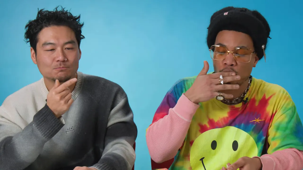 Close shot of two hosts eating small crispy pieces, tasting the delicate layered snack against a blue background