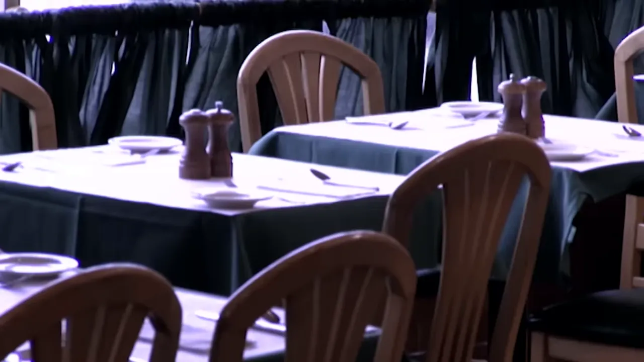 Empty restaurant tables set with plates, cutlery and pepper mills on green tablecloths