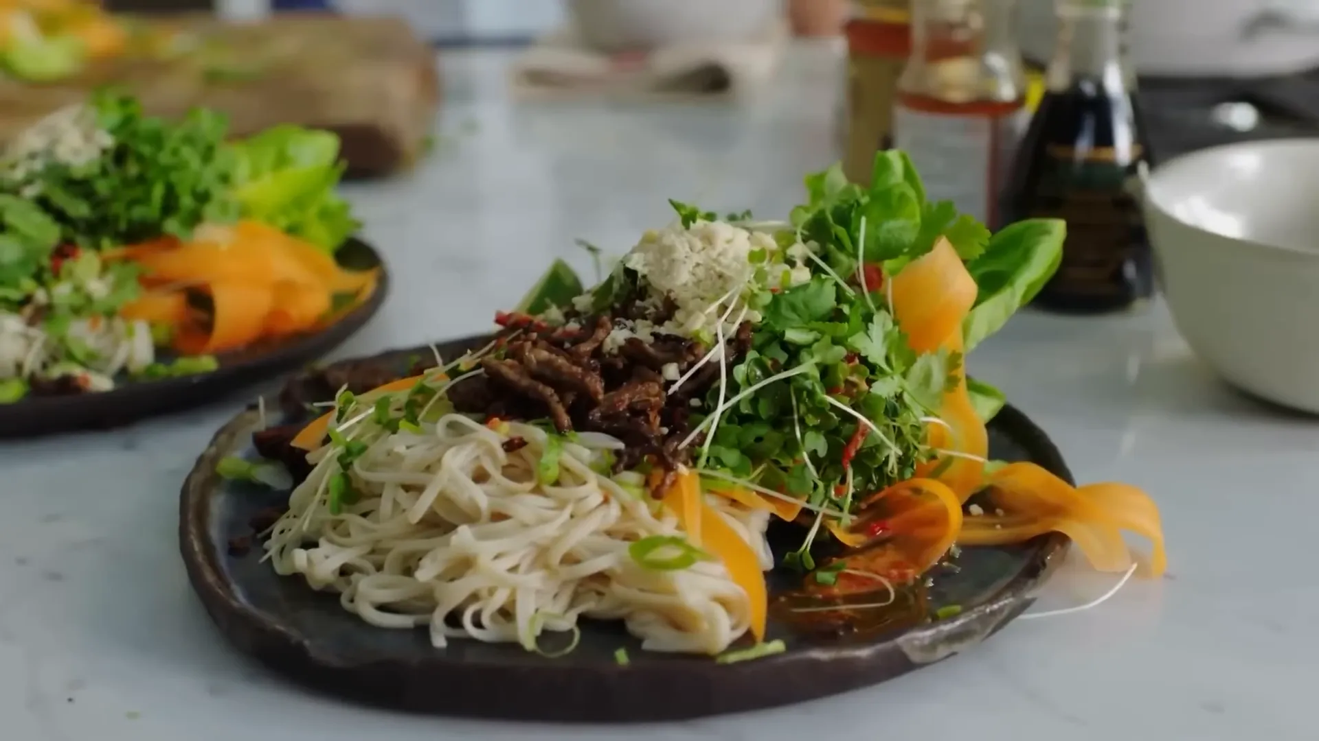 Asian-style crispy beef being sprinkled over noodles and salad