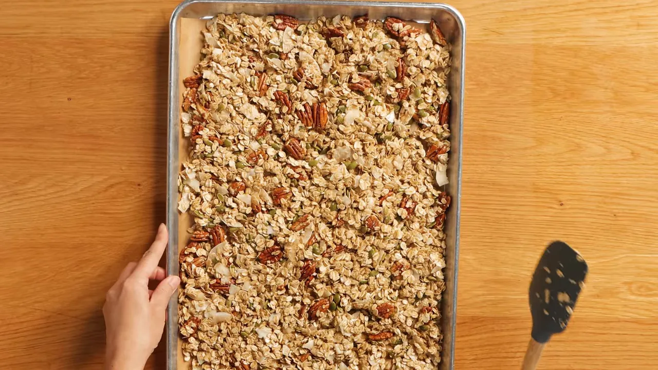 Top-down view of a full sheet pan of baked granola with pecans, pepitas, and coconut chips