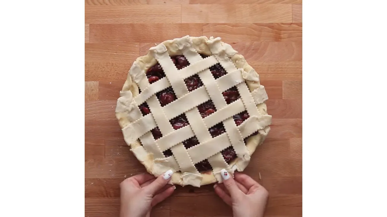Finished lattice cherry pie on a wooden board, hands holding the pie at the bottom