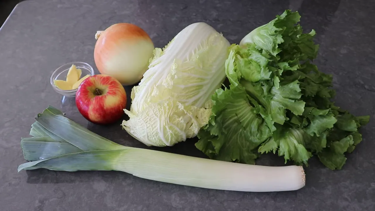Leek, napa cabbage, escarole, onion, apple and butter on a dark countertop prepared as soup ingredients