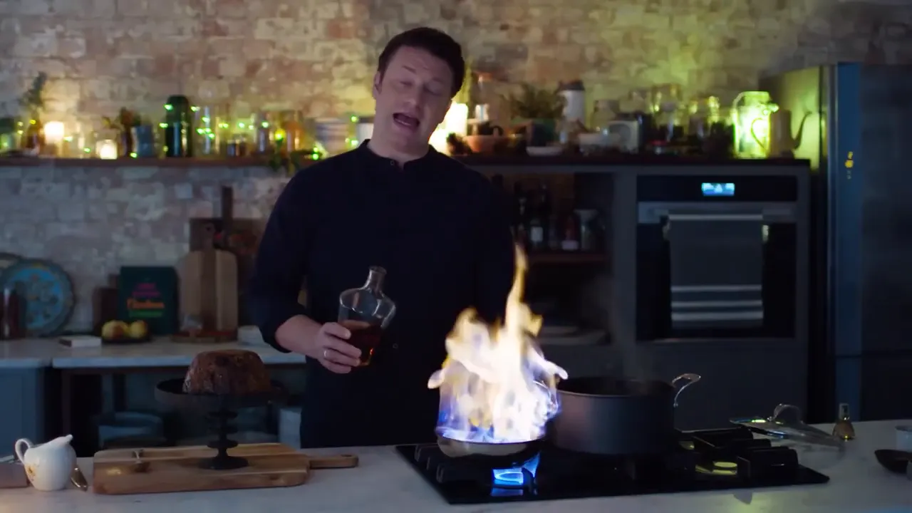 plated pudding on the counter while a tall blue and orange flame rises from a pan during a flaming demonstration