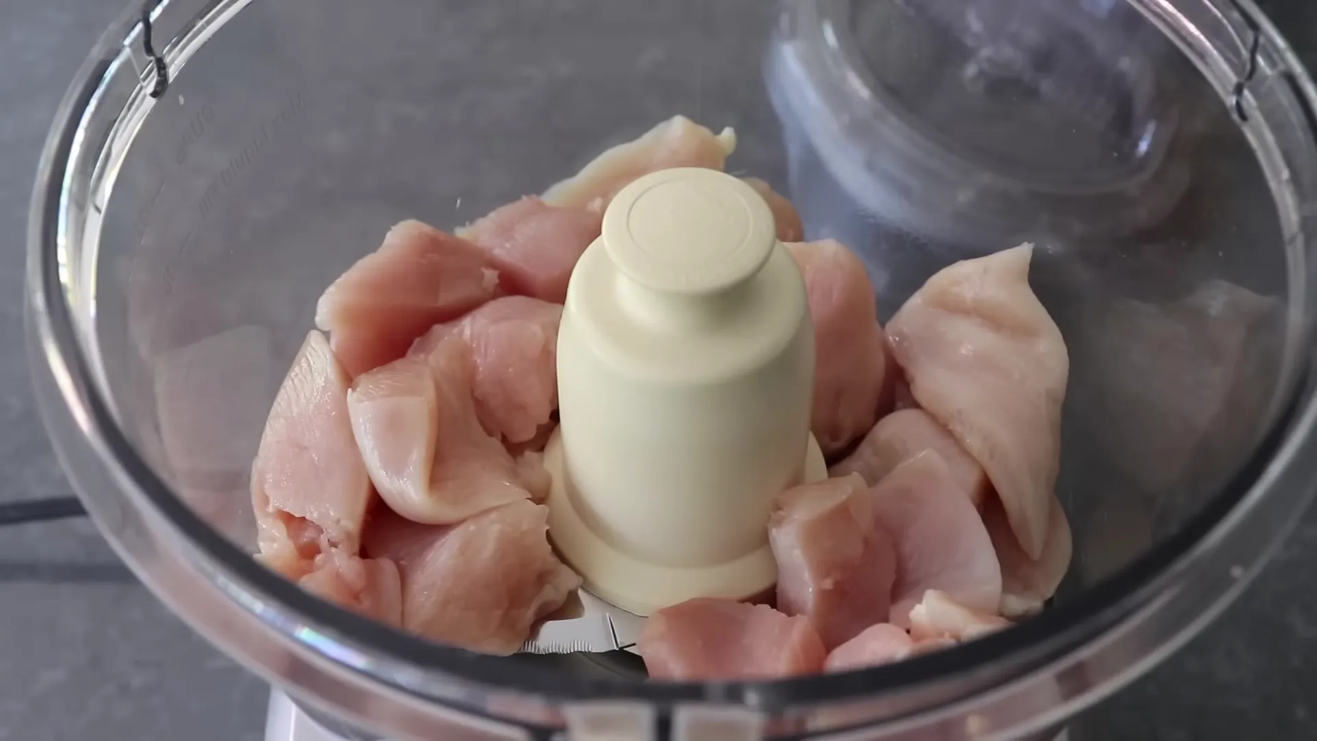 Boneless skinless chicken breasts being added to a food processor