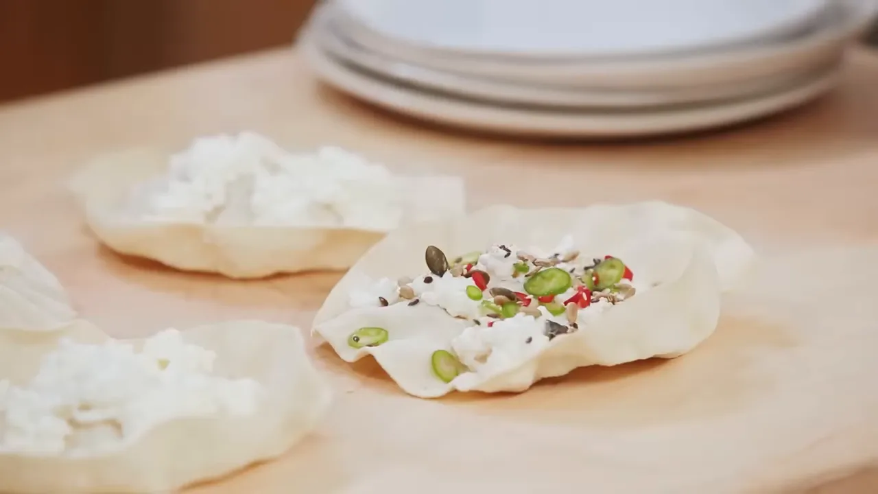 Three toasted poppadoms topped with cottage cheese, sliced chili and mixed seeds on a wooden board, close-up and clear.