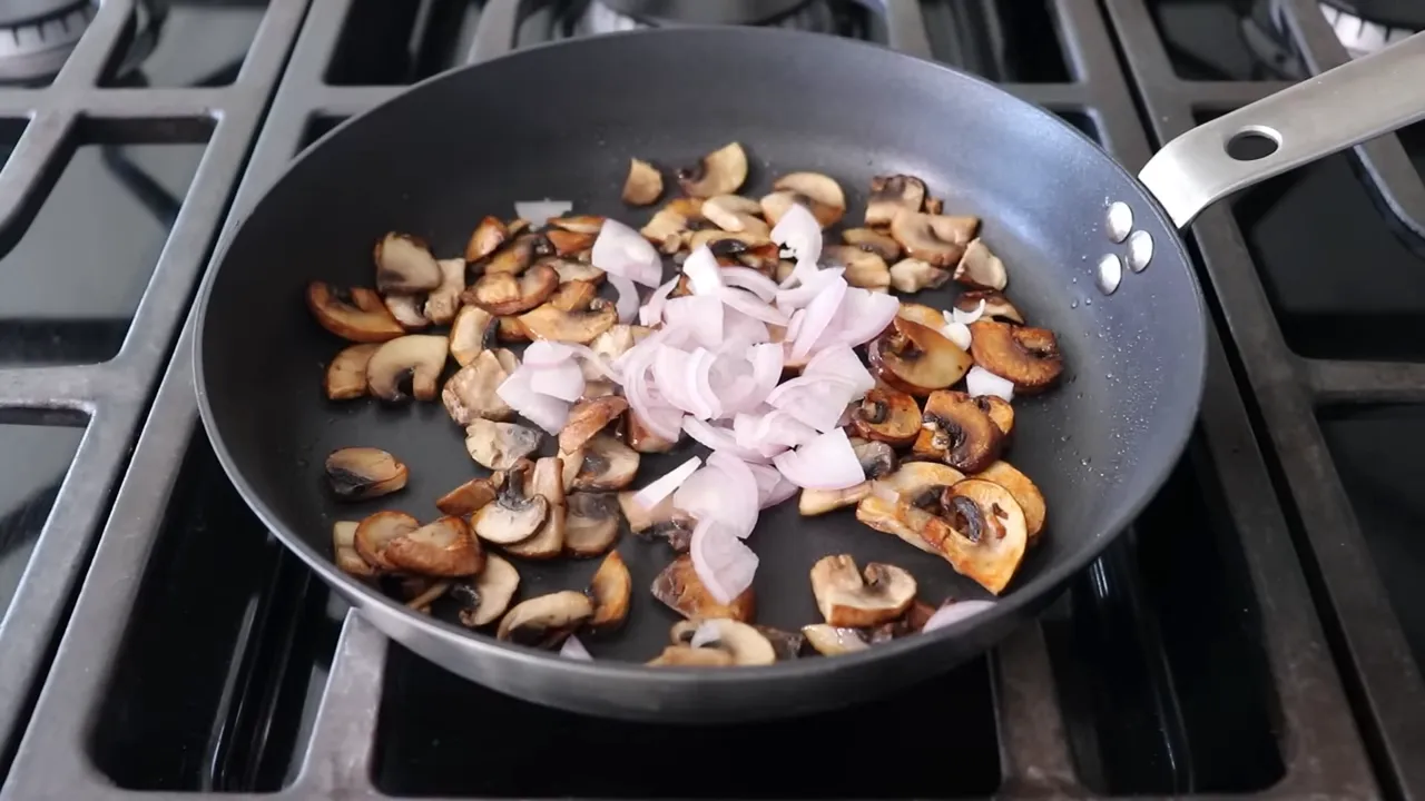 Thinly sliced shallot added on top of browned mushrooms in a frying pan
