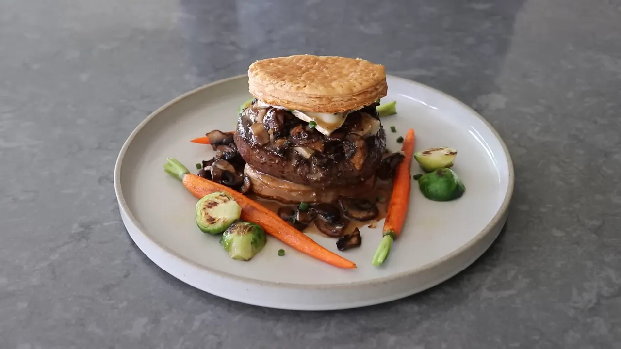 Centered Peek‑A‑Boo beef Wellington with mushroom duxelles, melted brie and puff pastry on a grey plate with carrots and brussels sprouts