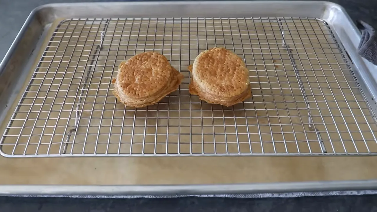 Two golden-brown puff pastry discs cooling on a wire rack over a baking sheet.