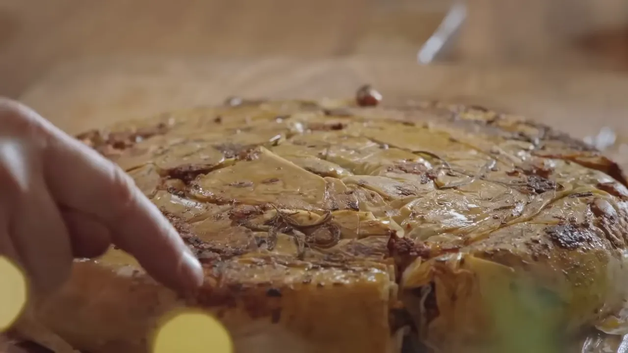 close-up of a baked filo pie with a finger lifting a slice to show layers and filling