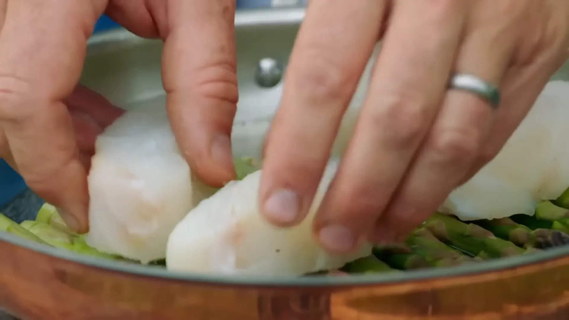 Seasoned cod fillets resting on asparagus in a pan