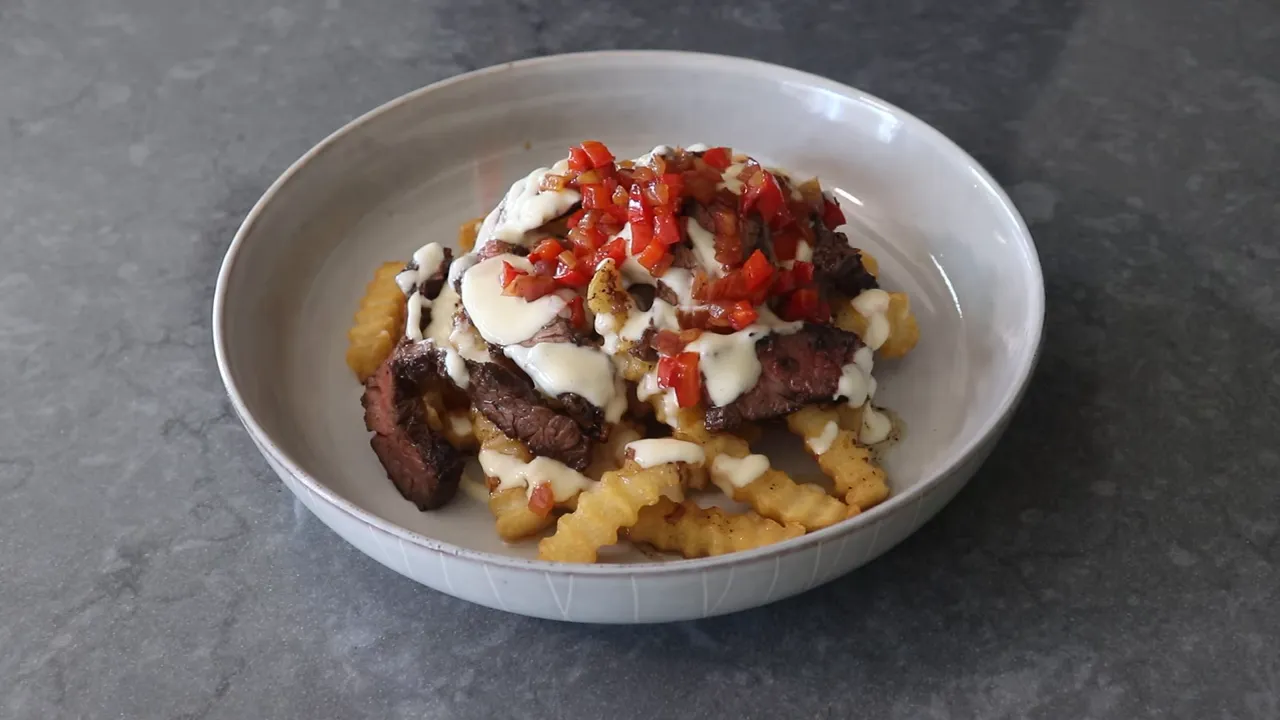 Finished garlic steak fries: crinkle-cut fries with sliced steak, melted cheese and red pepper relish in a bowl