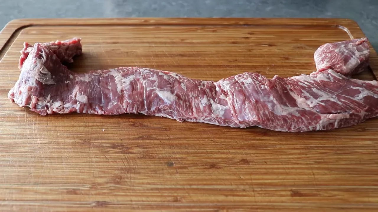 whole raw skirt steak laid flat on a wooden cutting board showing grain and marbling