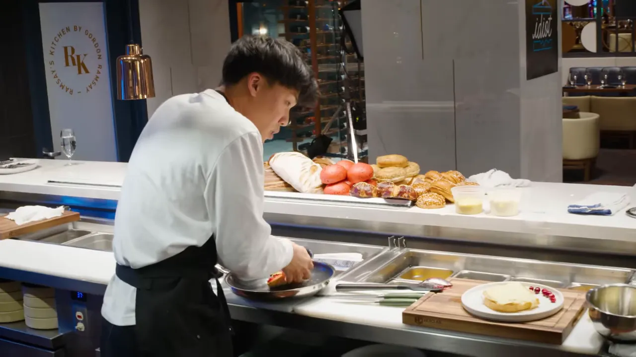 Chef finishing a turkey sandwich in a pan with a plated sandwich and cranberries on the counter