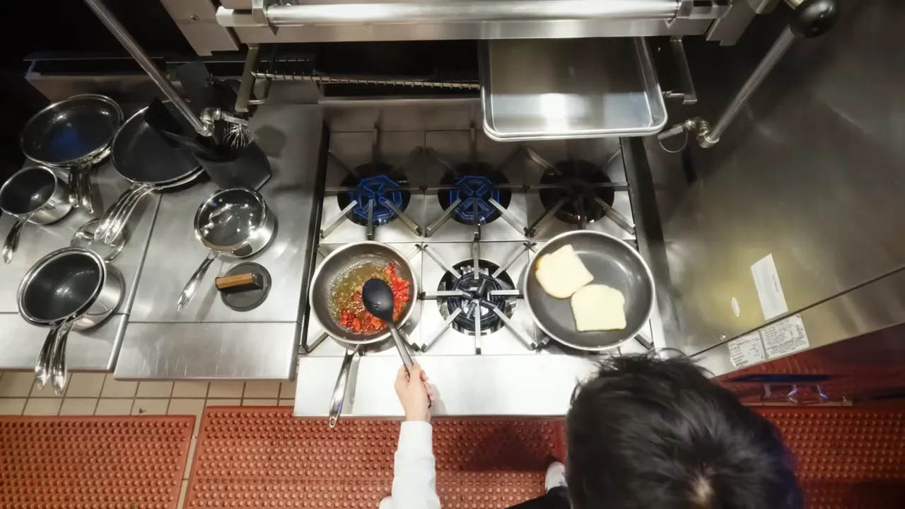 Top-down view of a stovetop with two slices of bread toasting in one pan and a simmering sauce in another