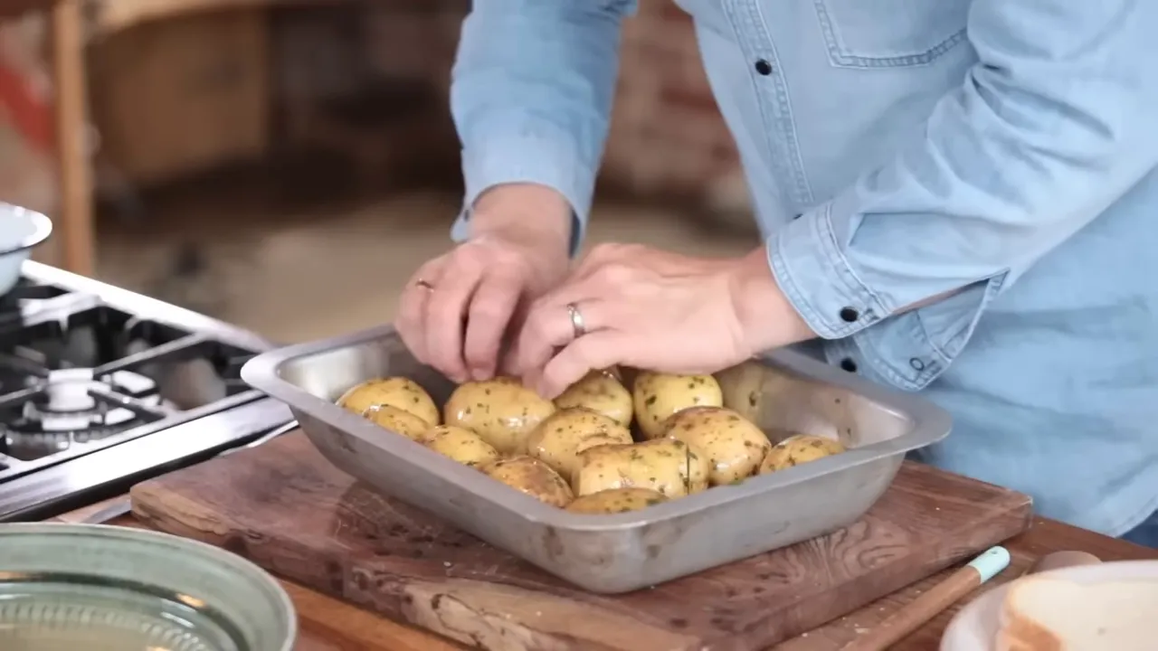 Close-up of hands arranging seasoned parboiled potatoes in a metal roasting tray