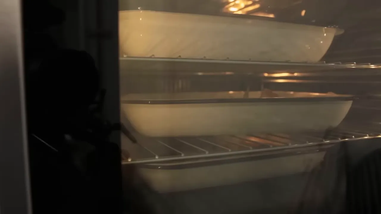 Two roasting trays of potatoes inside an oven viewed through the glass door