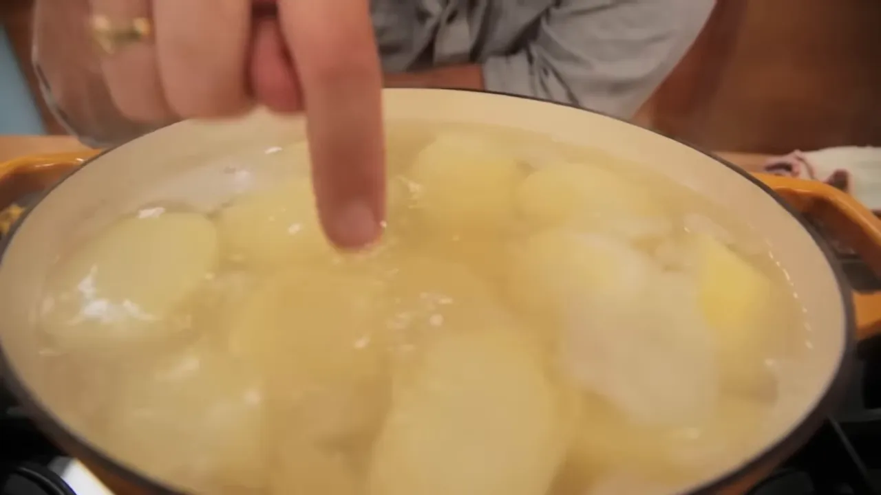 Finger pressing a parboiled potato in a pot to test tenderness