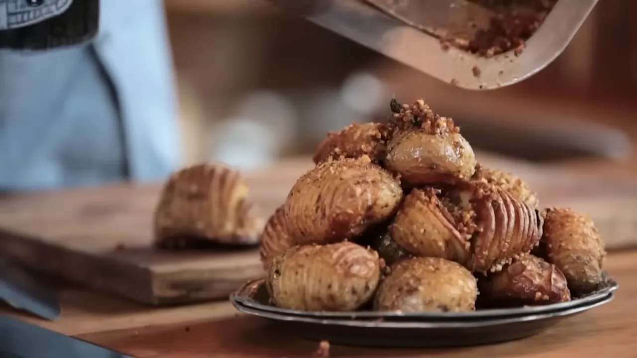 Close-up of a plate piled with crisp hasselback roast potatoes being finished with a crunchy topping