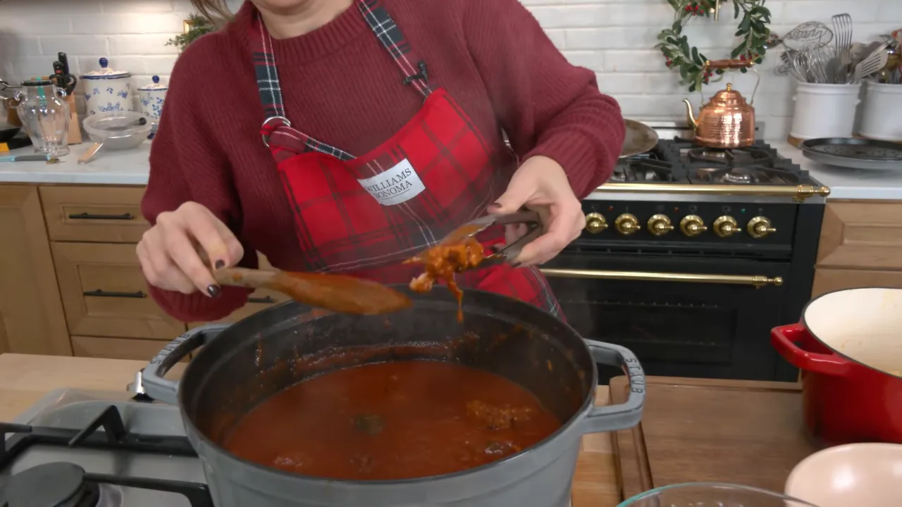 Close-up of a meatball being lifted from tomato sauce with tongs over a Dutch oven