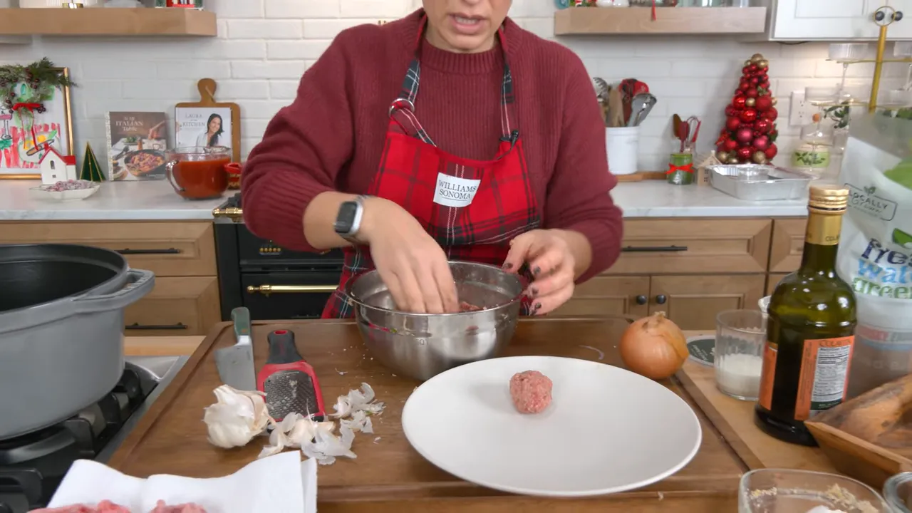 A single formed meatball on a plate next to the mixing bowl as the cook reaches in