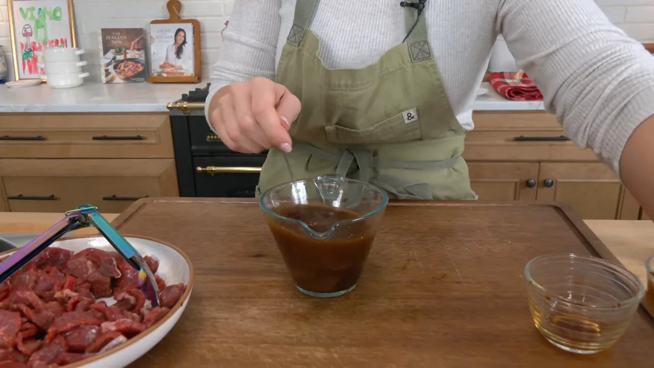 glass measuring cup of beef and broccoli stir-fry sauce being whisked on a cutting board with sliced beef to the side
