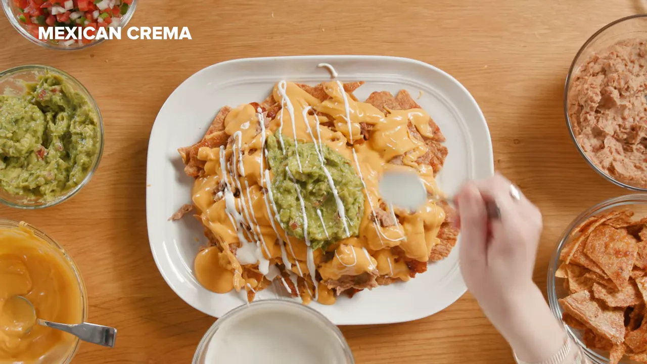 Top-down view of chicken nachos while crema is drizzled over the plate