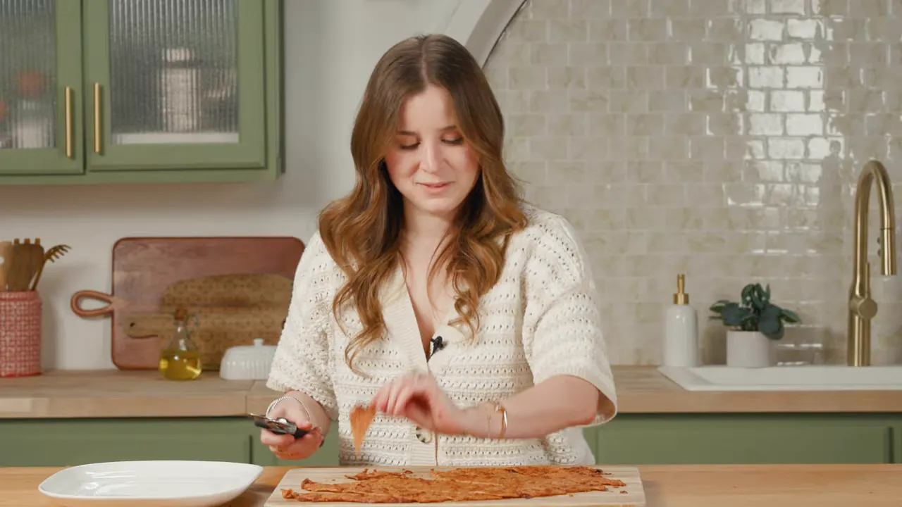Hands cutting a baked ground-chicken sheet into chip-shaped pieces on a cutting board
