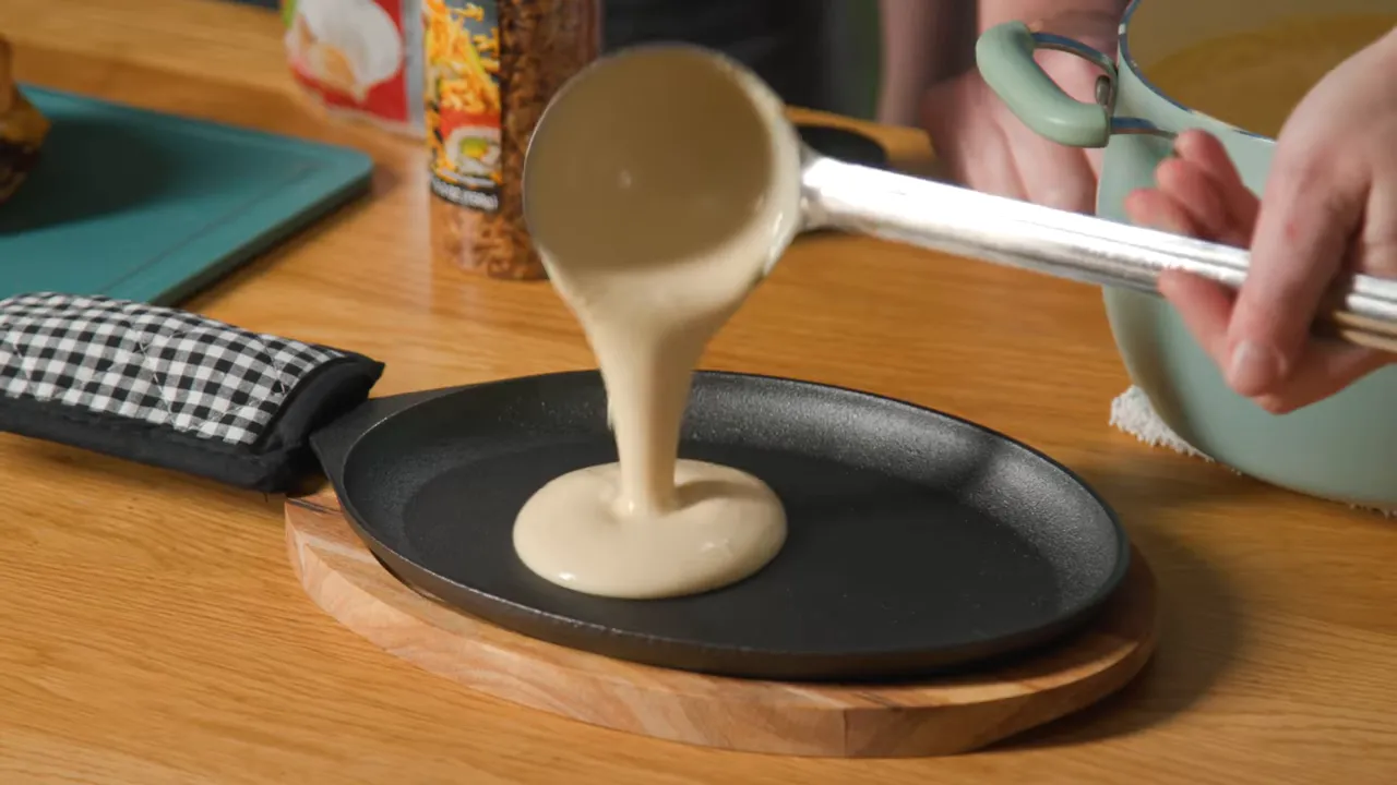 Ladle pouring creamy white cheese sauce onto a hot sizzle plate