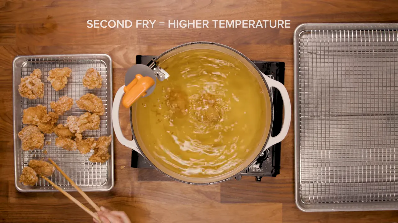 Top-down view of a pot of oil with fried chicken on a tray and overlaid text 'SECOND FRY = HIGHER TEMPERATURE'.