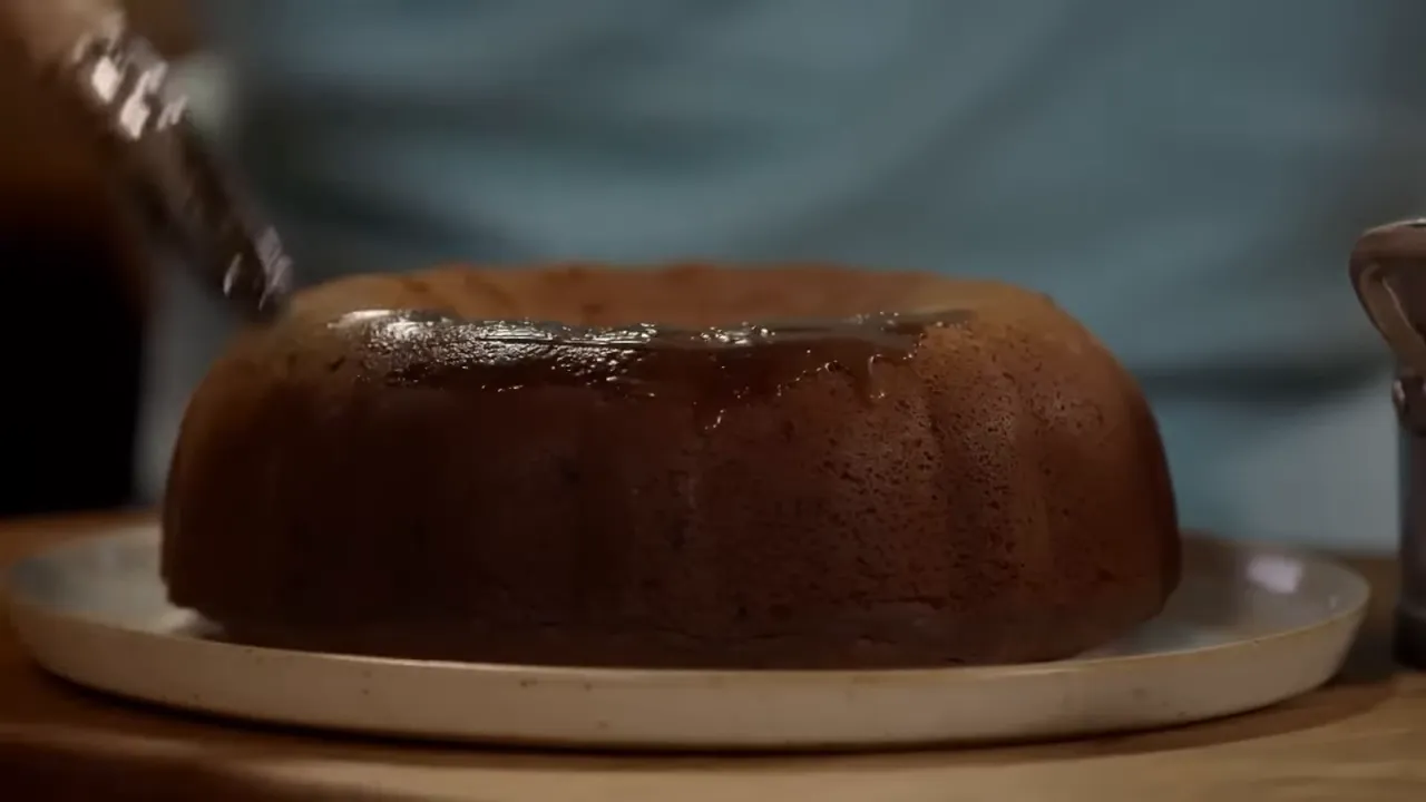 Bundt-style sticky toffee pudding on a plate being brushed with toffee sauce
