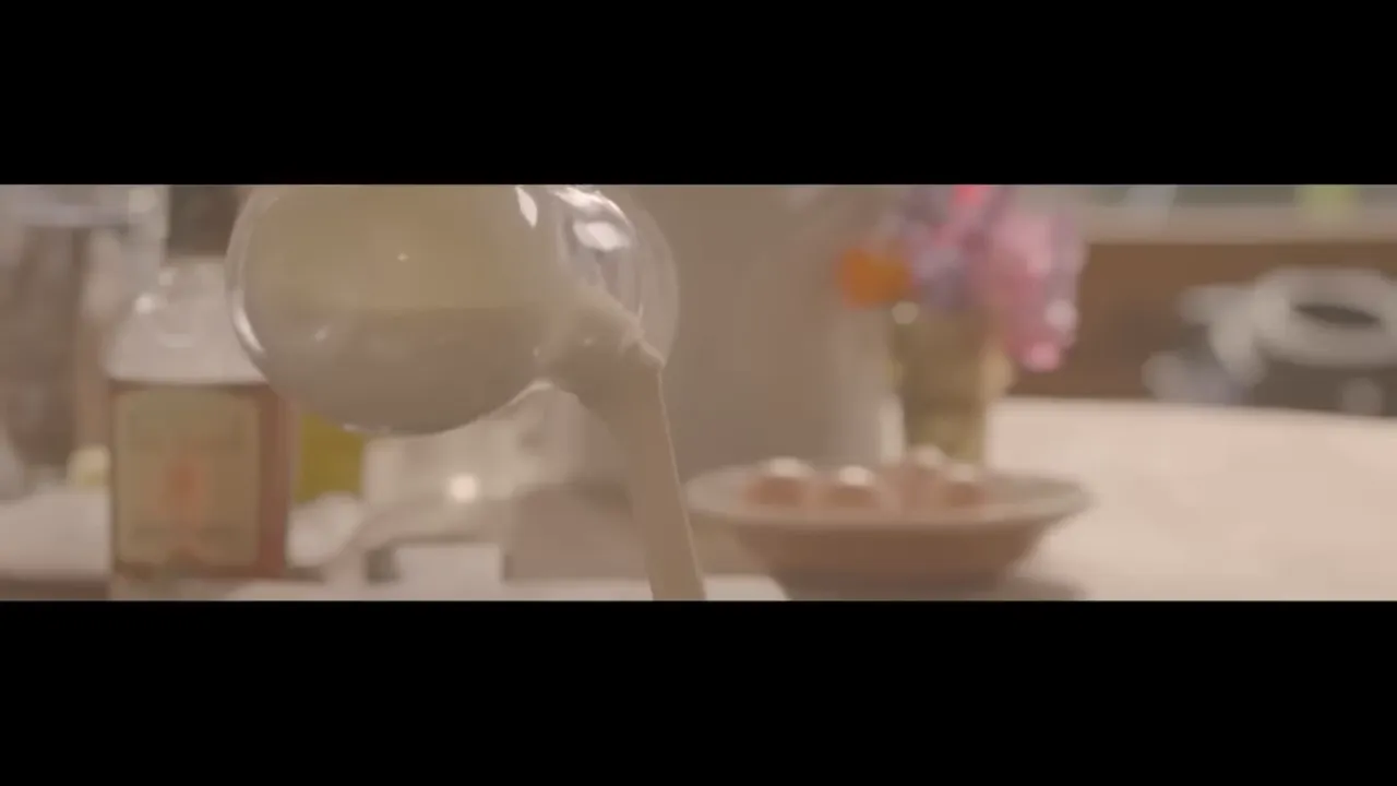Glass jug pouring double cream into a sauce with a steady stream and soft kitchen background